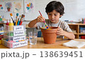 Child painting terracotta flower pot at craft table in classroom with focused boy and paint jars 138639451