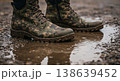 Camouflaged boots in puddle with wet gravel texture and clear reflection in rainy daylight scene 138639452