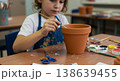 Child painting terracotta flower pot at desk with paintbrush and clay pot in school art project 138639455