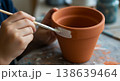 Child painting terracotta flower pot close view of hand holding brush painting rim on clay pot 138639464