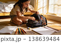 Girl organizing backpack on floor with sunlight on rug and papers spread around open bag in focus 138639484
