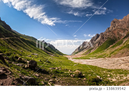 Panoramic view of Mynzhylky valley and Tuyuk-Su Gate in Tian Shan, Kazakhstan. Green slopes, rocky peaks and mountain road under blue sky. 138639542