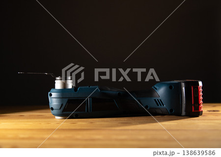 Sleek power tool Multi-cutter showcased on a wooden surface against a dark backdrop, emphasizing its design and functionality, copy space Sleek power tool Multi-cutter showcased on a wooden surface against a dark backdrop, emphasizing its design and functionality, copy space 138639586
