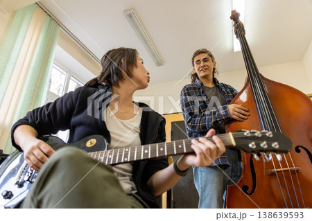 A female guitarist and a male double bass player looking at each other while discussing a song in a college music room. 138639593
