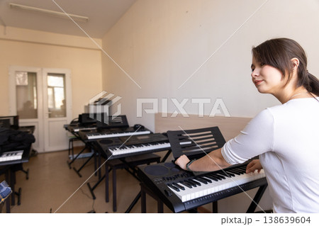 Young woman adjusting a synthesizer in a study hall filled with various musical keyboards. Young woman adjusting a synthesizer in a study hall filled with various musical keyboards. 138639604