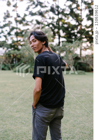 Relaxed young man turns to look back in a green park Relaxed young man turns to look back in a green park 138639612