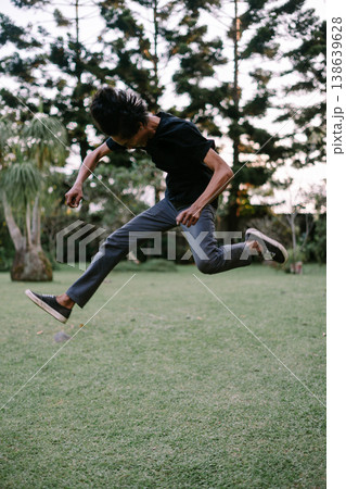 Energetic Young Person Leaping Mid-Air Outdoors in a Green Park 138639628