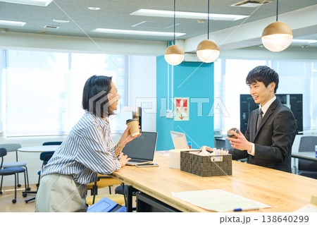 オフィスの休憩室でコーヒーを片手に笑顔でコミュニケーションをとる男女 オフィスの休憩室でコーヒーを片手に笑顔でコミュニケーションをとる男女 138640299