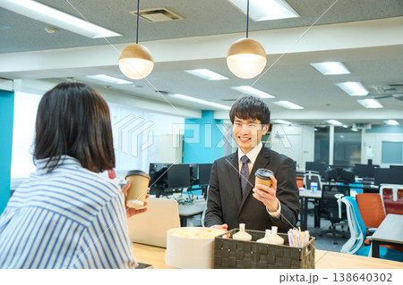 オフィスのカフェスペースでコーヒーを飲みながら同僚と談笑する男性社員 138640302