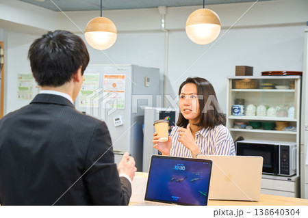 オフィスの給湯室で同僚の男性と楽しく談笑する笑顔のビジネスウーマン オフィスの給湯室で同僚の男性と楽しく談笑する笑顔のビジネスウーマン 138640304
