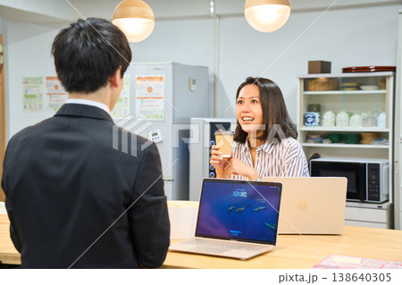 オフィスの給湯室で同僚の男性と楽しく談笑する笑顔のビジネスウーマン オフィスの給湯室で同僚の男性と楽しく談笑する笑顔のビジネスウーマン 138640305