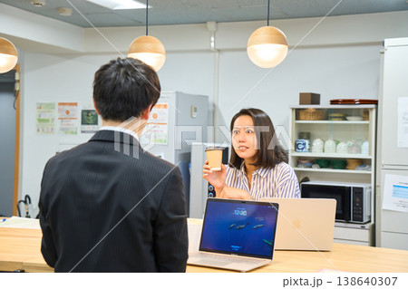 オフィスの給湯室で同僚の男性と楽しく談笑する笑顔のビジネスウーマン オフィスの給湯室で同僚の男性と楽しく談笑する笑顔のビジネスウーマン 138640307