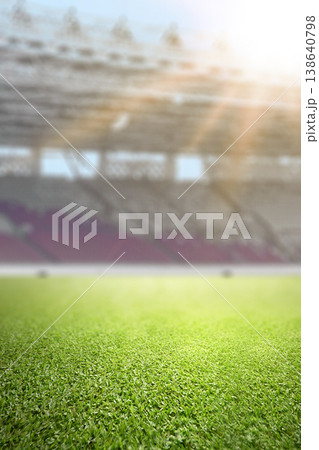 Close-up of lush green grass on a professional soccer field with a blurred stadium and bright sunlight in the background. Ideal for sport-themed designs Close-up of lush green grass on a professional soccer field with a blurred stadium and bright sunlight in the background. Ideal for sport-themed designs 138640798