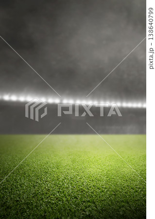 A dramatic vertical shot of a lush green grass field in a sports stadium at night, featuring bright floodlights and a smoky atmosphere 138640799