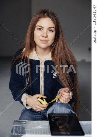 Female interior designer measuring wall with yellow tape measure in a minimalist empty room during renovation. Female interior designer measuring wall with yellow tape measure in a minimalist empty room during renovation. 138641347