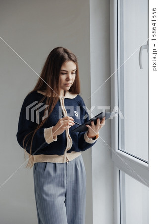 Young female interior designer working on digital tablet with stylus, planning home renovation project by the window. Young female interior designer working on digital tablet with stylus, planning home renovation project by the window. 138641356