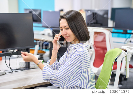 オフィスのデスクでスマートフォンで通話する女性社員の横顔 オフィスのデスクでスマートフォンで通話する女性社員の横顔 138641573