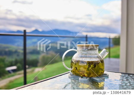 Tea being served in a glass teapot with a mountain view in the background on a cloudy day Tea being served in a glass teapot with a mountain view in the background on a cloudy day 138641679