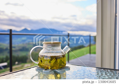 Tea being served in a glass teapot with a mountain view in the background on a cloudy day 138641685