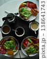 Breakfast spread featuring avocado toast, coffee, and sides on a round table in the morning light 138641743
