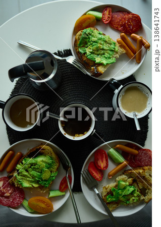 Breakfast spread featuring avocado toast, coffee, and sides on a round table in the morning light Breakfast spread featuring avocado toast, coffee, and sides on a round table in the morning light 138641743
