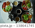 Breakfast spread featuring avocado toast, coffee, and sides on a round table in the morning light 138641745