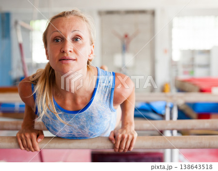 Woman gymnast performs complex acrobatic exercise on parallel bars in gym Woman gymnast performs complex acrobatic exercise on parallel bars in gym 138643518
