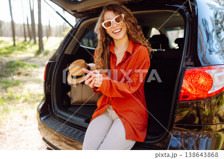 Happy woman enjoying nature while sitting in the trunk of her car during a solo trip. Road trip 138643868