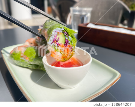 茹で海老と野菜を巻いた生春巻き。スイートチリソースをつけて食べる様子。 茹で海老と野菜を巻いた生春巻き。スイートチリソースをつけて食べる様子。 138644207