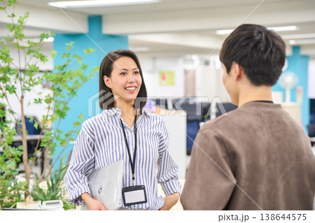 オフィスでデバイスを持ち同僚の男性と笑顔で話す女性社員 138644575