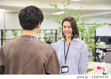 オフィスでデバイスを持ち同僚の男性と笑顔で話す女性社員 138644576