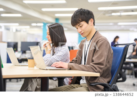 フリーアドレスのオフィスで並んでパソコン作業をする男女の社員 フリーアドレスのオフィスで並んでパソコン作業をする男女の社員 138644652