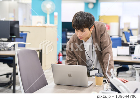 フリーアドレスのオフィスで立ったままノートパソコンの画面を確認する若い男性社員 フリーアドレスのオフィスで立ったままノートパソコンの画面を確認する若い男性社員 138644780