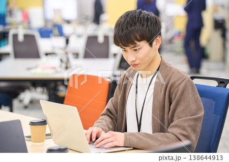 オフィスでコーヒーを傍らにノートパソコンでの作業に集中する若い男性社員 オフィスでコーヒーを傍らにノートパソコンでの作業に集中する若い男性社員 138644913