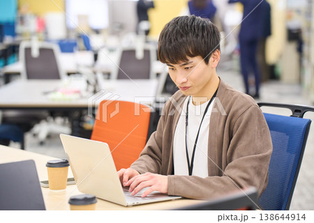 オフィスでコーヒーを傍らにノートパソコンでの作業に集中する若い男性社員 オフィスでコーヒーを傍らにノートパソコンでの作業に集中する若い男性社員 138644914