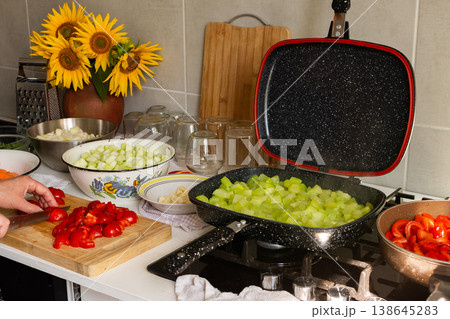 A woman cuts tomatoes on a wooden board surrounded by fresh vegetables while preparing squash caviar for winter canning in her kitchen A woman cuts tomatoes on a wooden board surrounded by fresh vegetables while preparing squash caviar for winter canning in her kitchen 138645283