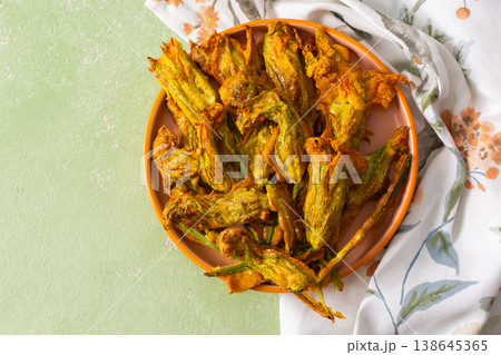 Golden-brown deep-fried zucchini flowers are arranged on a vibrant plate. The dish is set on a floral-patterned napkin, enhancing its appetizing appearance Golden-brown deep-fried zucchini flowers are arranged on a vibrant plate. The dish is set on a floral-patterned napkin, enhancing its appetizing appearance 138645365