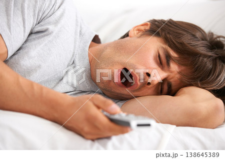 Tv, yawn and tired man in bed with remote control for streaming movies in his home. Fatigue, relax and morning lazy male in a bedroom with television, show or film while on vacation in his house 138645389