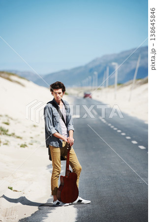 Musician, travel and man with a guitar on a road trip, journey or tour in the countryside on highway. Guitarist, trekking and portrait of guy waiting on street for a car, van or transportation 138645846