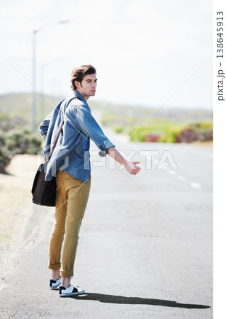 Man, travel and musician with a guitar on a road trip, journey or tour in the countryside on highway. Guitarist, trekking and portrait of guy waiting on street for a car, van or transportation 138645913