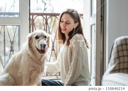 Woman petting golden retriever dog in front of a balcony door Woman petting golden retriever dog in front of a balcony door 138646214