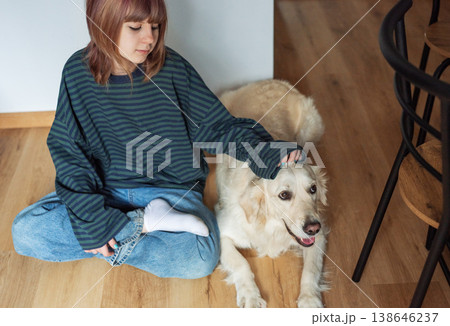 Girl petting golden retriever dog on home floor 138646237