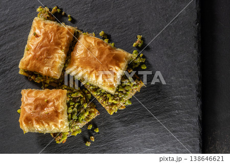 Traditional pistachio baklava on granite. Close-up of pistachio baklava on granite background. Turkish dessert baklava with pistachios. Pistachio baklava on stone surface. Traditional pistachio baklava on granite. Close-up of pistachio baklava on granite background. Turkish dessert baklava with pistachios. Pistachio baklava on stone surface. 138646621