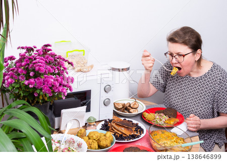 A person sits at a kitchen table eating food. Dishes with different homemade meals are arranged around her. Flowers add color to the table setting. A microwave is nearby A person sits at a kitchen table eating food. Dishes with different homemade meals are arranged around her. Flowers add color to the table setting. A microwave is nearby 138646899