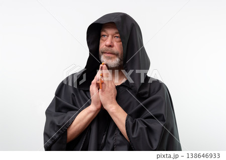 Elderly monk in black robe with folded hands holding rosary. Elderly monk in black robe with folded hands holding rosary. 138646933
