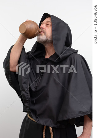 Male monk drinking from clay jug wearing black robe Male monk drinking from clay jug wearing black robe 138646956