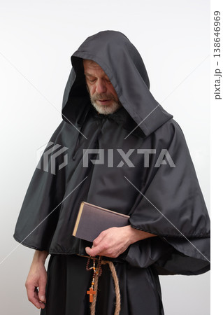 Male monk standing holding book and rosary wearing black robe. Male monk standing holding book and rosary wearing black robe. 138646969