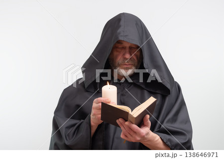 Bearded monk in hood holding candle and reading text. 138646971
