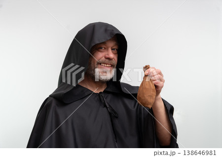 An old monk in a black robe with a bag of money on a white background. An old monk in a black robe with a bag of money on a white background. 138646981