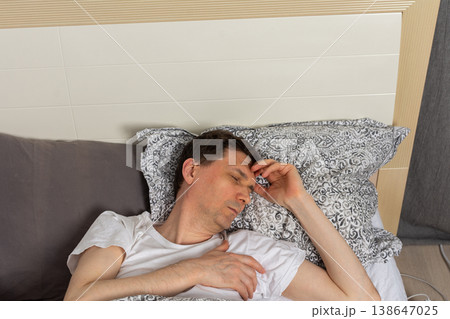 A 53-year-old man sleeps in his bedroom on a bed. He rests on blankets and pillows, holding his head while dozing off during the night A 53-year-old man sleeps in his bedroom on a bed. He rests on blankets and pillows, holding his head while dozing off during the night 138647025